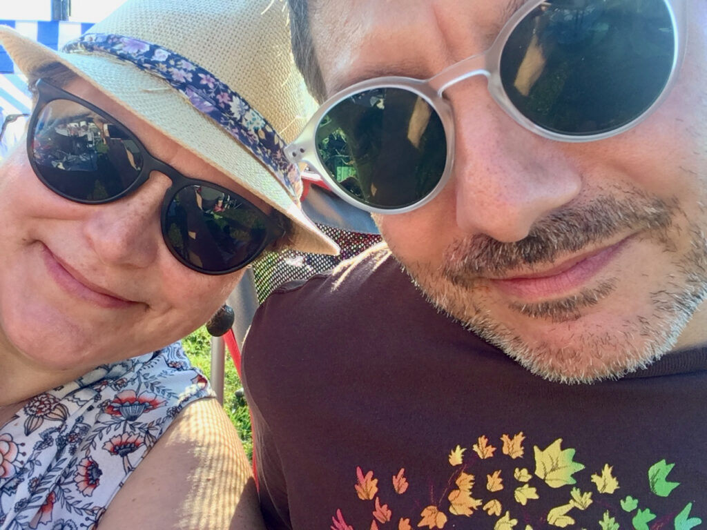 Close up of a man and woman's faces. They are leaning into each other. Both are wearing sunglasses.