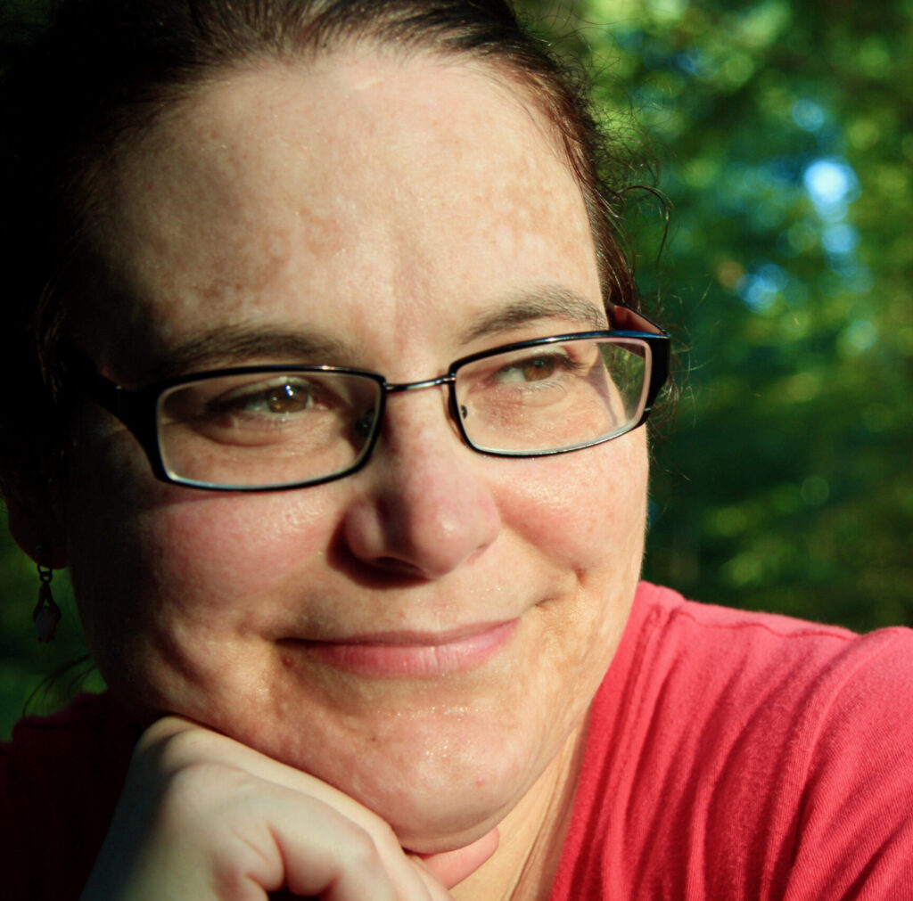 Close-up of a woman with glasses wearing a pink shirt.